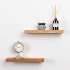 Wooden shelves with a clock, plant, and diffuser on a white wall.