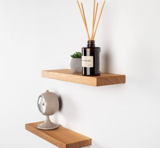 Wooden shelves with a diffuser, clock, and plant on a white wall