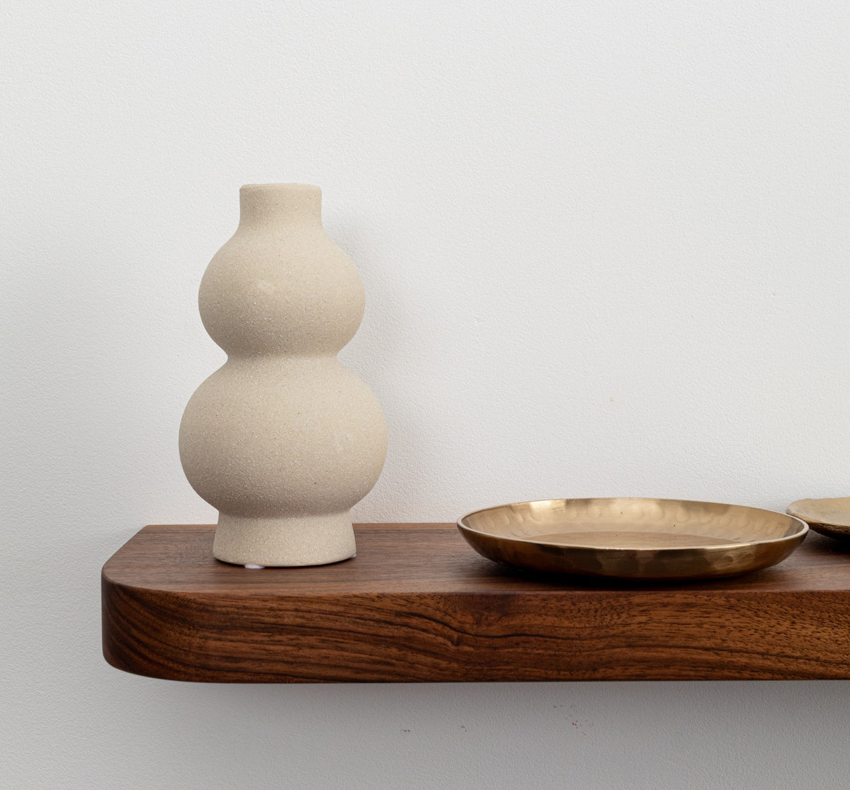 Beige ceramic vase on a wooden shelf with a plain background