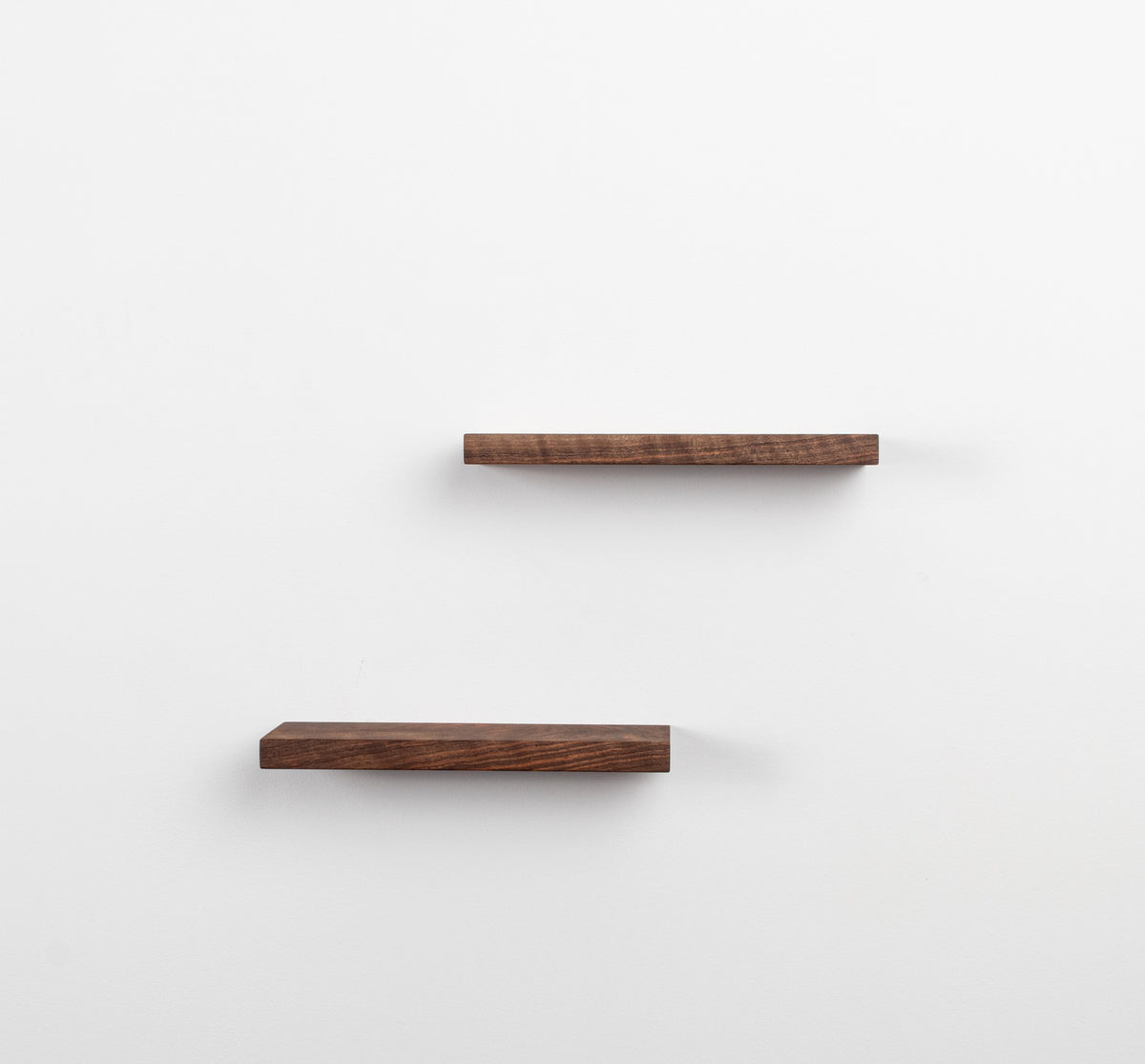 Two wooden shelves on a white wall