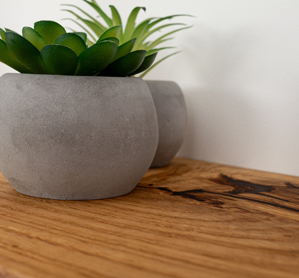 Two gray concrete planters with green plants on a wooden surface.
