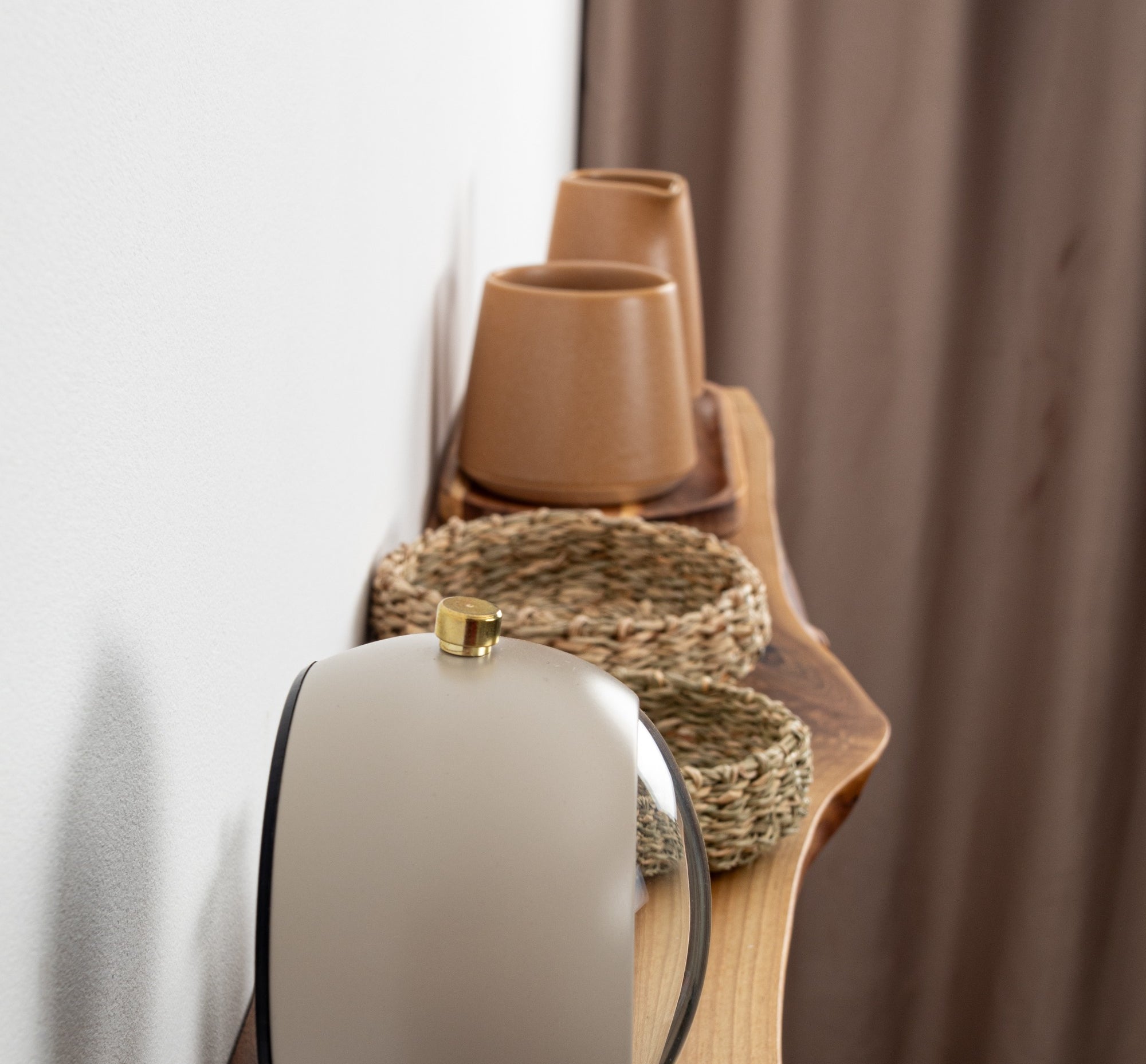 Decorative items including a white vase, brown cups, and a woven basket on a wooden surface with a curtain in the background.