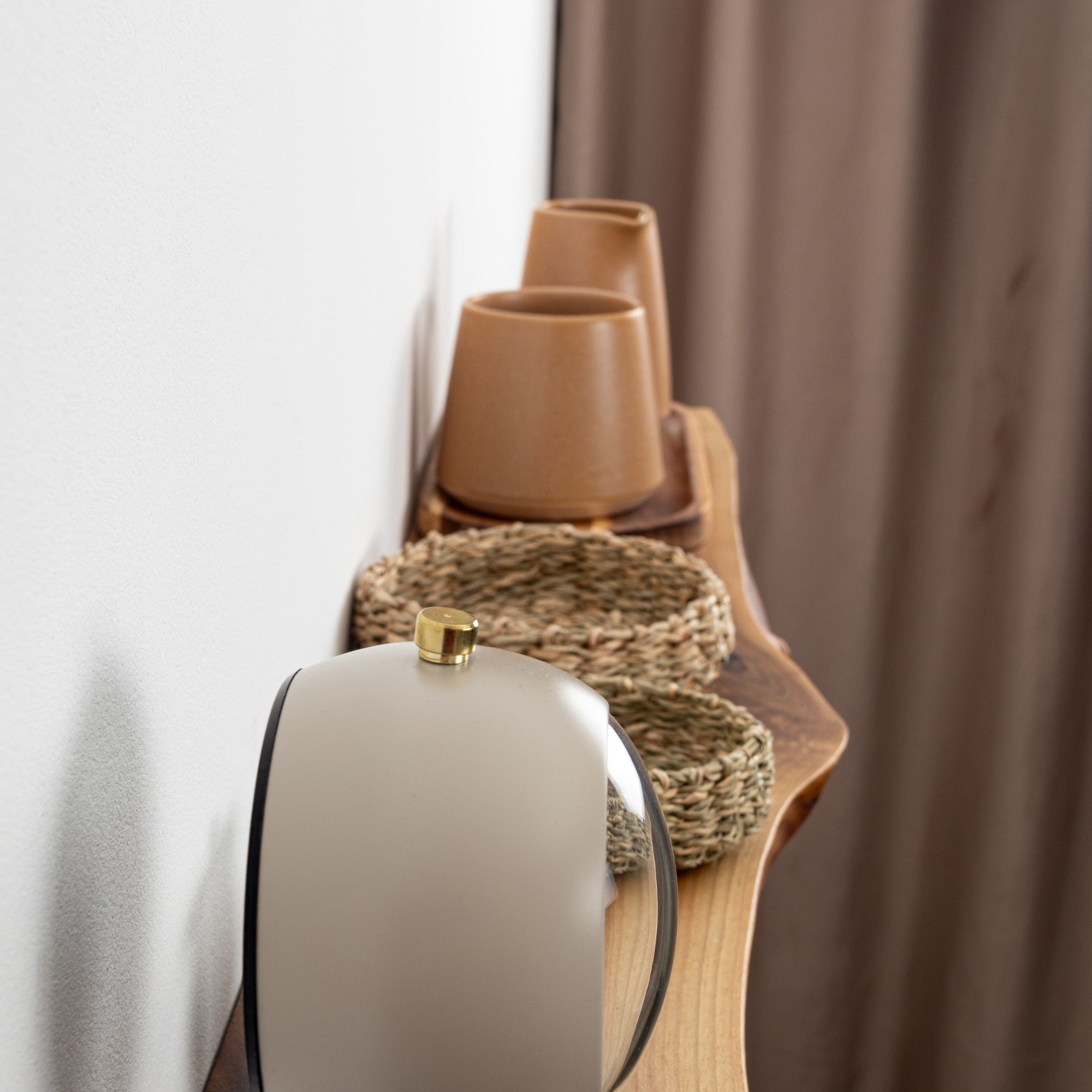 Decorative items including a white vase, brown cups, and a woven basket on a wooden surface with a curtain in the background.