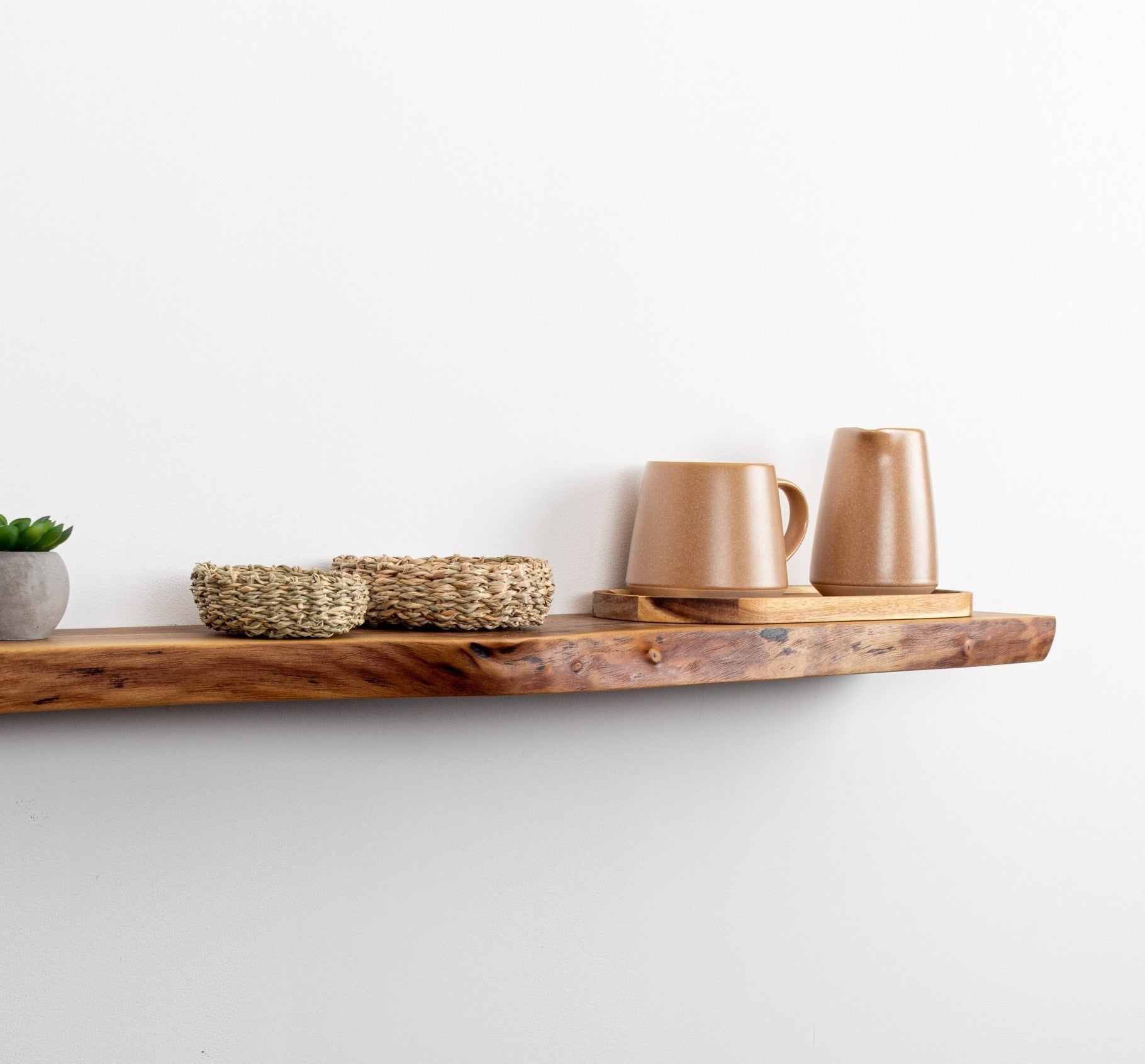 Wooden shelf with ceramic mugs and a woven basket on a white wall.