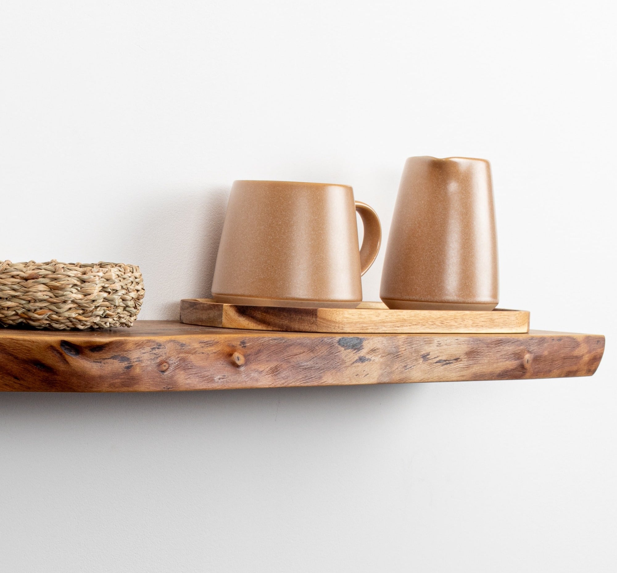 Two brown ceramic mugs on a wooden shelf against a white wall