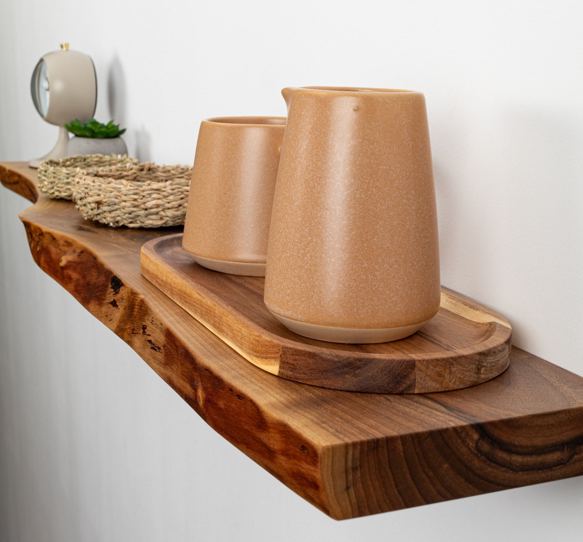 Two brown ceramic cups on a wooden shelf against a white wall.