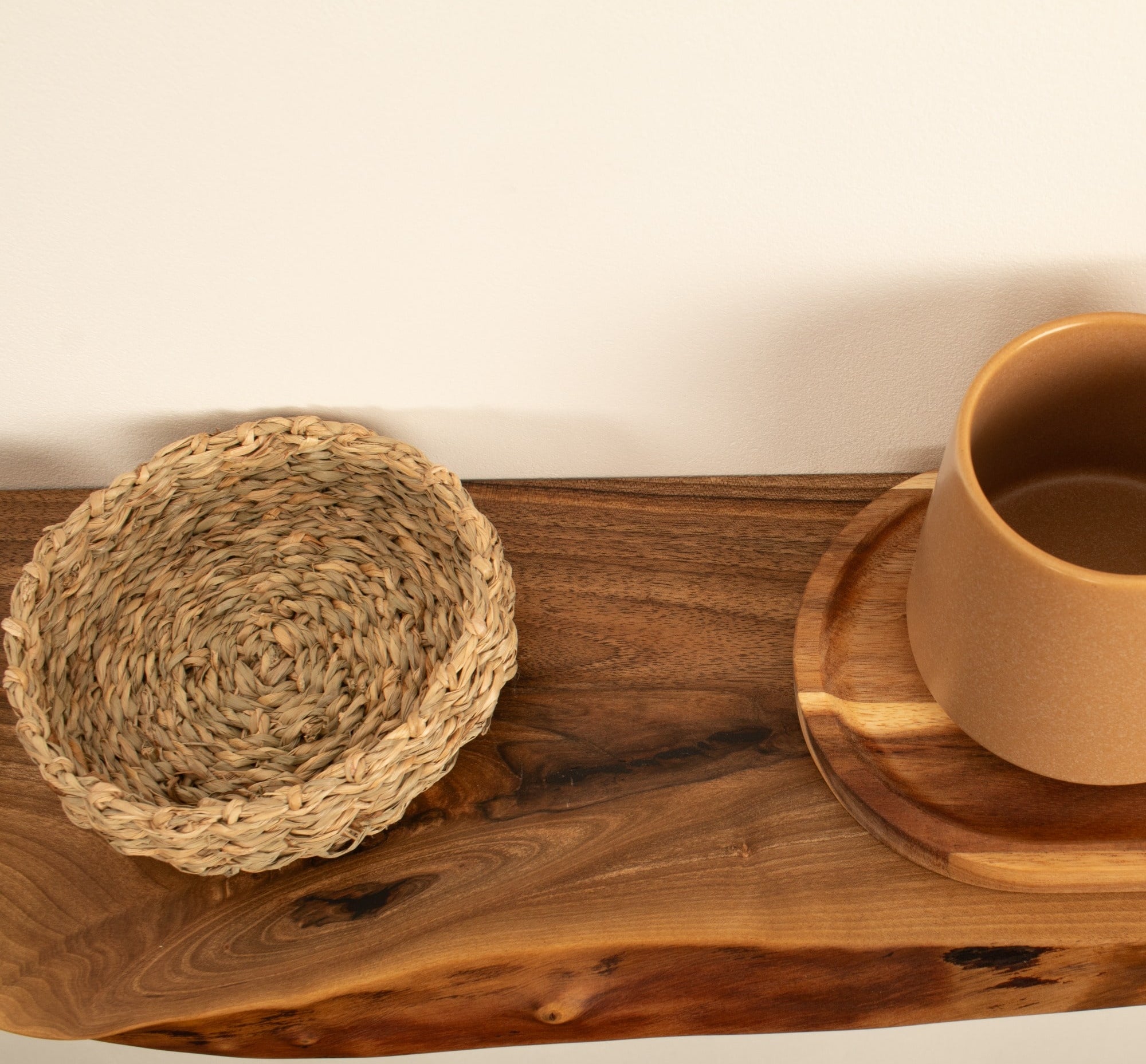 Brown ceramic cup on a wooden coaster with a woven mat on a wooden surface.