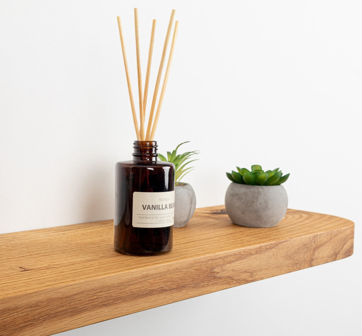 Vanilla reed diffuser on a wooden shelf with small plants