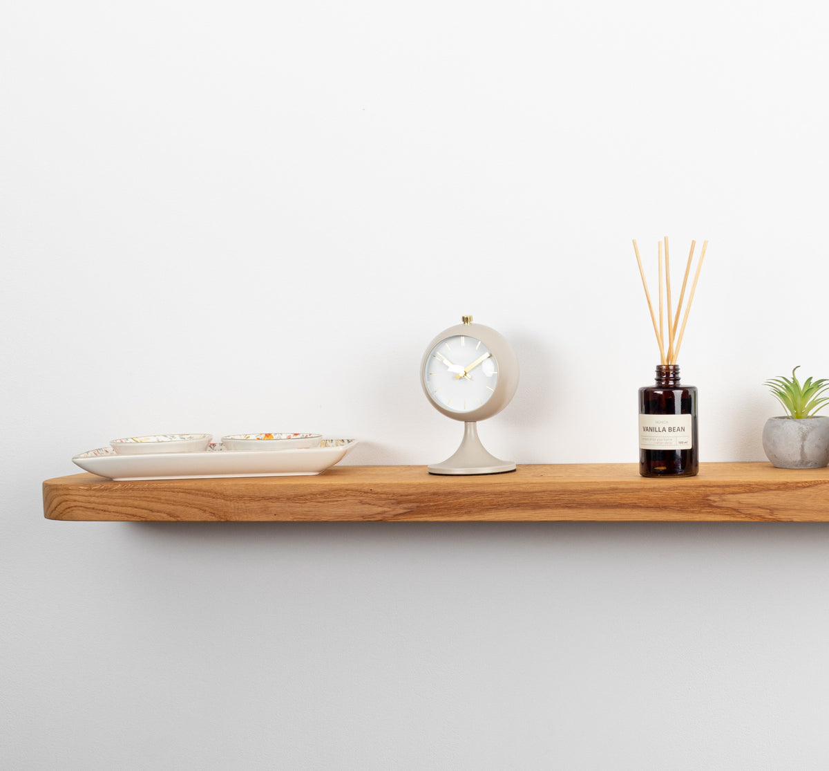 Wooden shelf with decorative items including a plant, bottle, and small clock on a white wall.