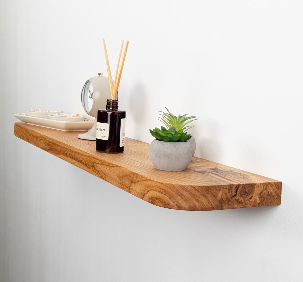 Wooden shelf with decorative items including a plant, diffuser, and bowls on a white wall.
