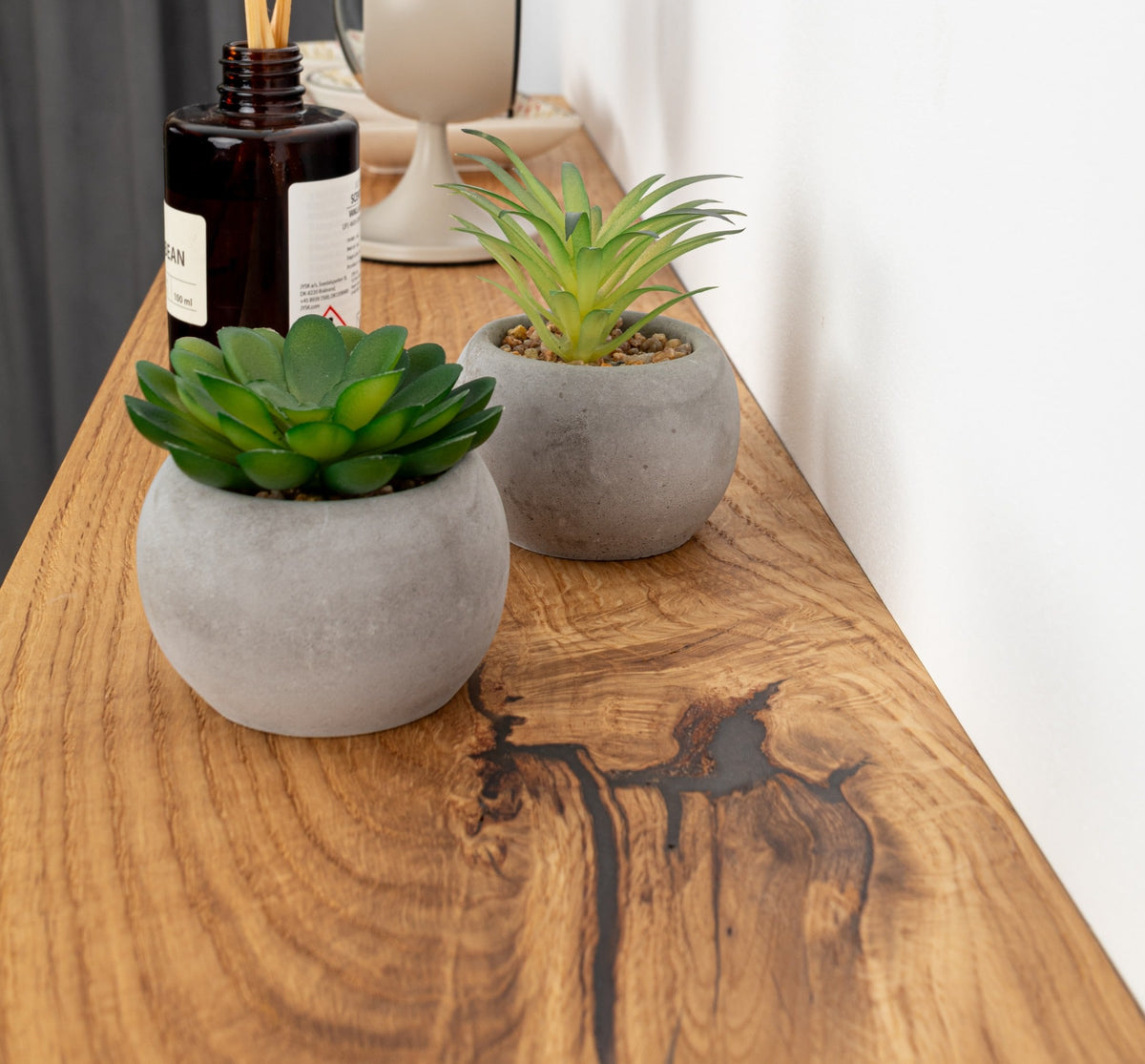Two small potted plants on a wooden surface with a bottle in the background.