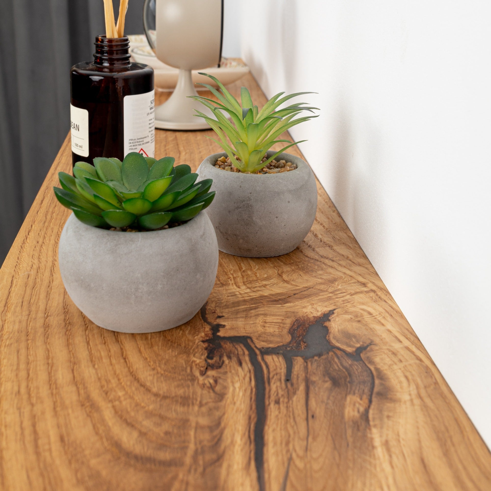 Two small potted plants on a wooden surface with a bottle in the background.