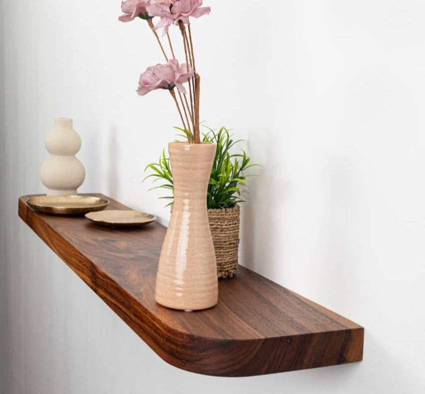 Wooden shelf with decorative items including a vase with pink flowers, a small plant, and a bowl on a white background.