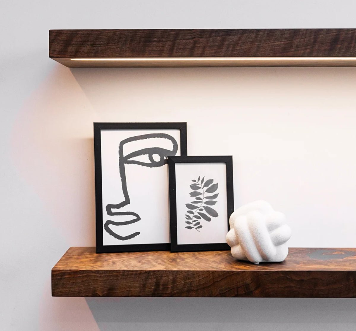 Wooden shelf with framed artwork and a white sculpture against a light wall.