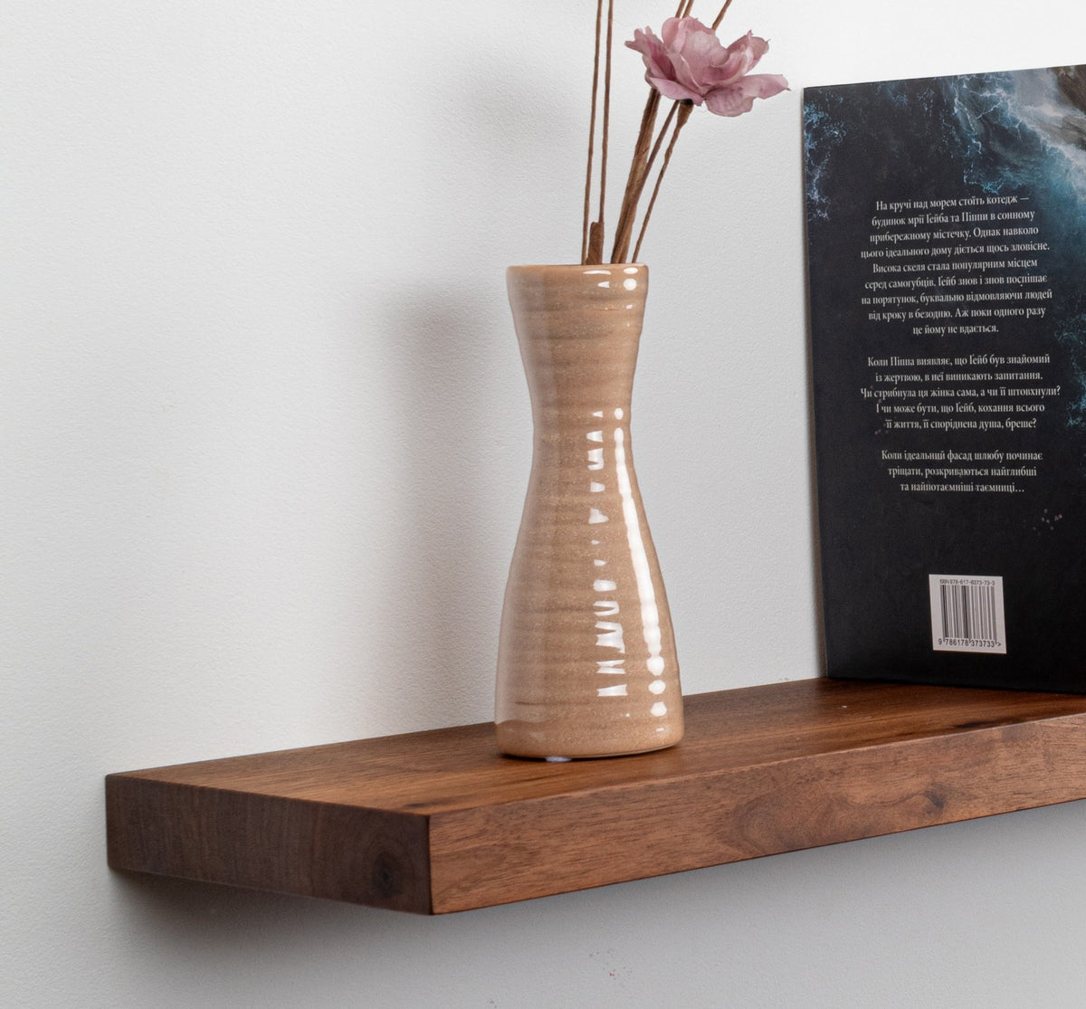 Wooden shelf with a ceramic vase and dried flowers against a white wall.