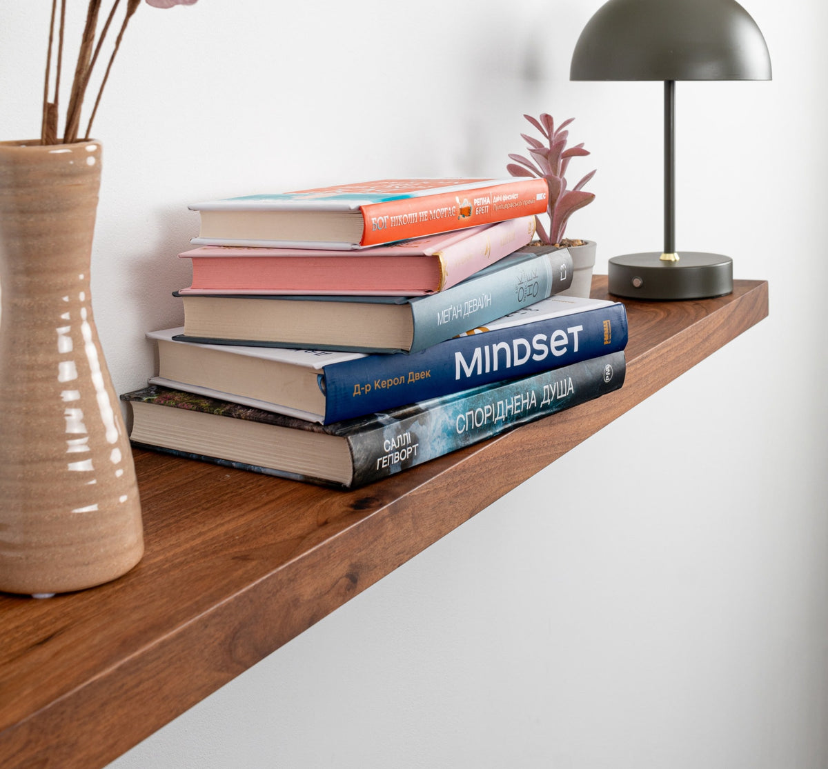 Wooden shelf with books, a vase, and a lamp against a white wall.