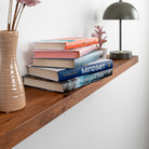 Wooden shelf with books, a vase, and a lamp against a white wall.