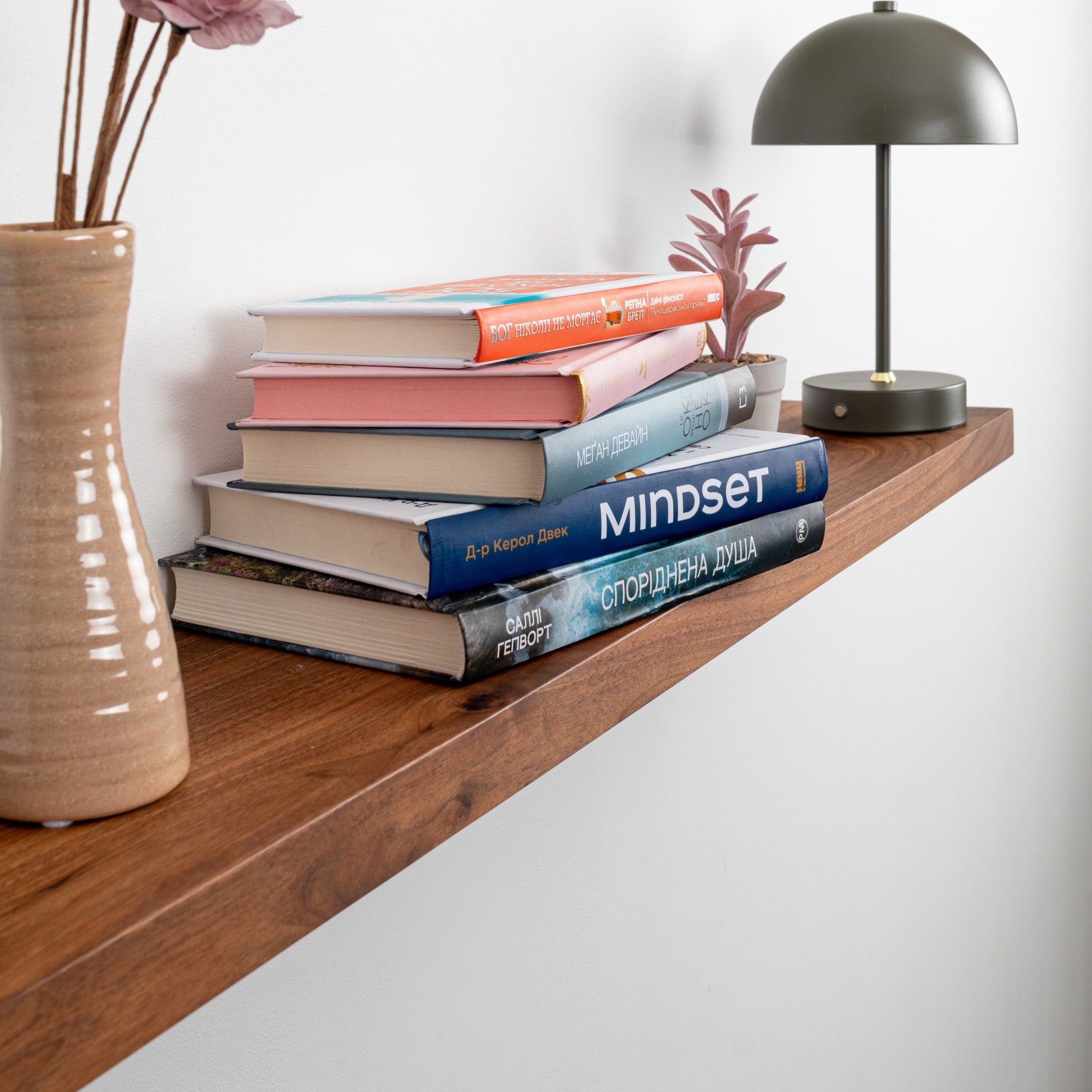 Wooden shelf with books, a vase, and a lamp against a white wall.