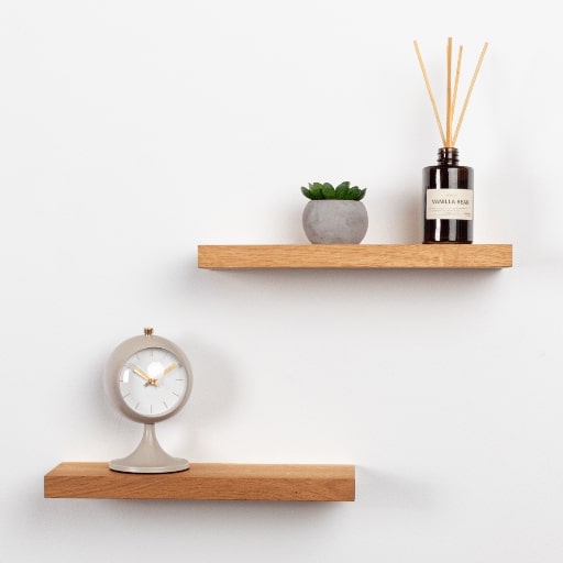 Wooden shelves with a clock, plant, and diffuser on a white wall.