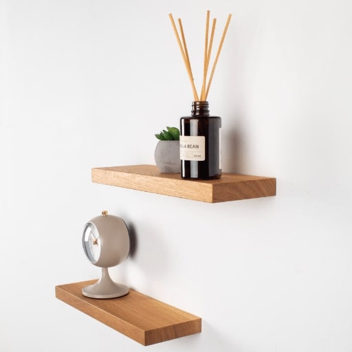 Wooden shelves with a diffuser, clock, and plant on a white wall