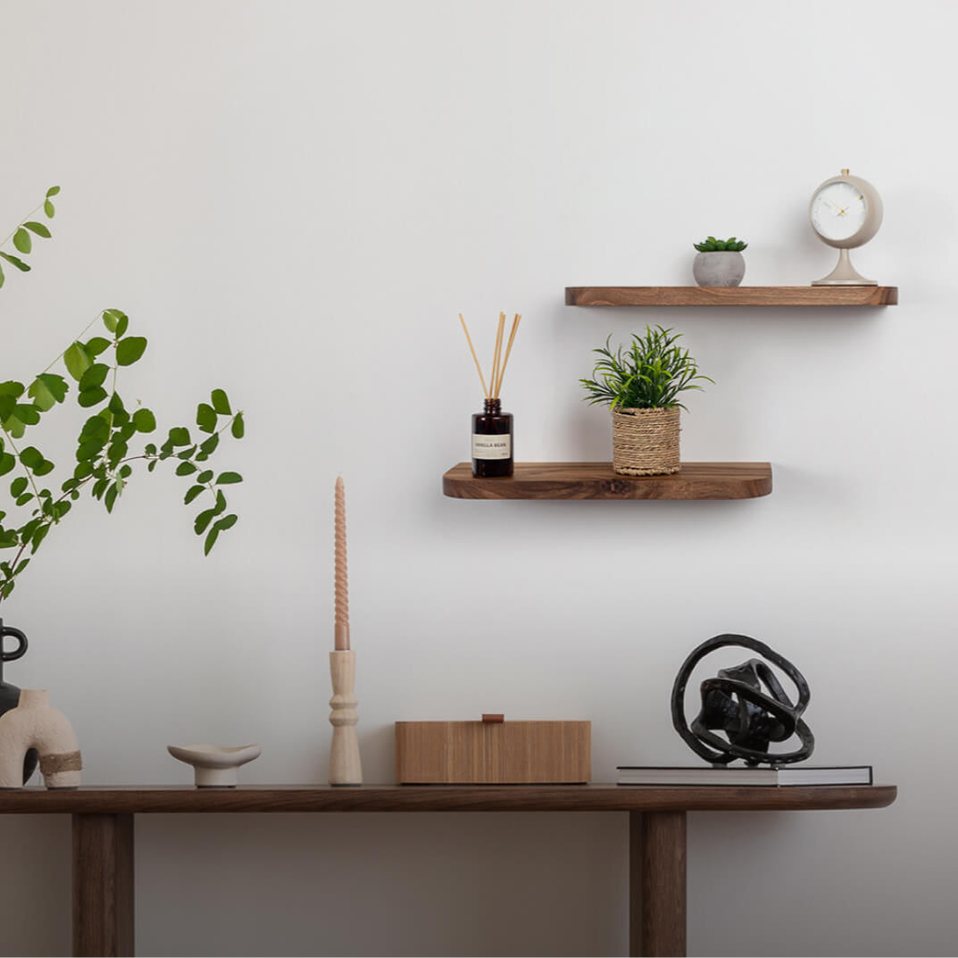 Wooden shelf with decorative items including a plant, candles, and a clock against a white wall.