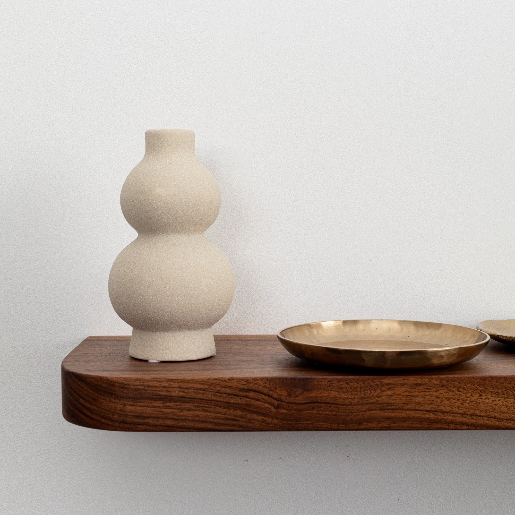 Beige ceramic vase on a wooden shelf with a plain background