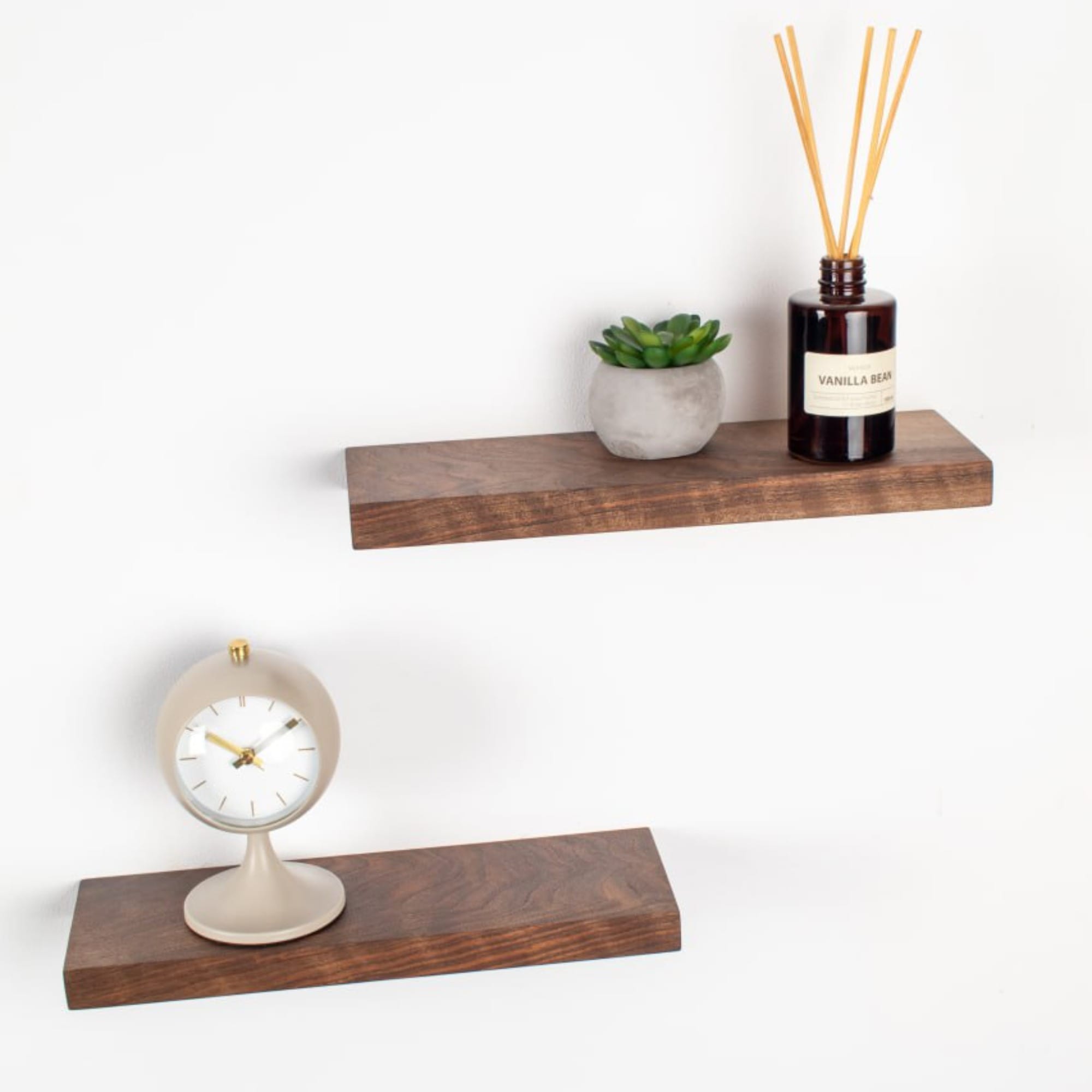 Wooden shelves with a clock, plant, and diffuser on a white background