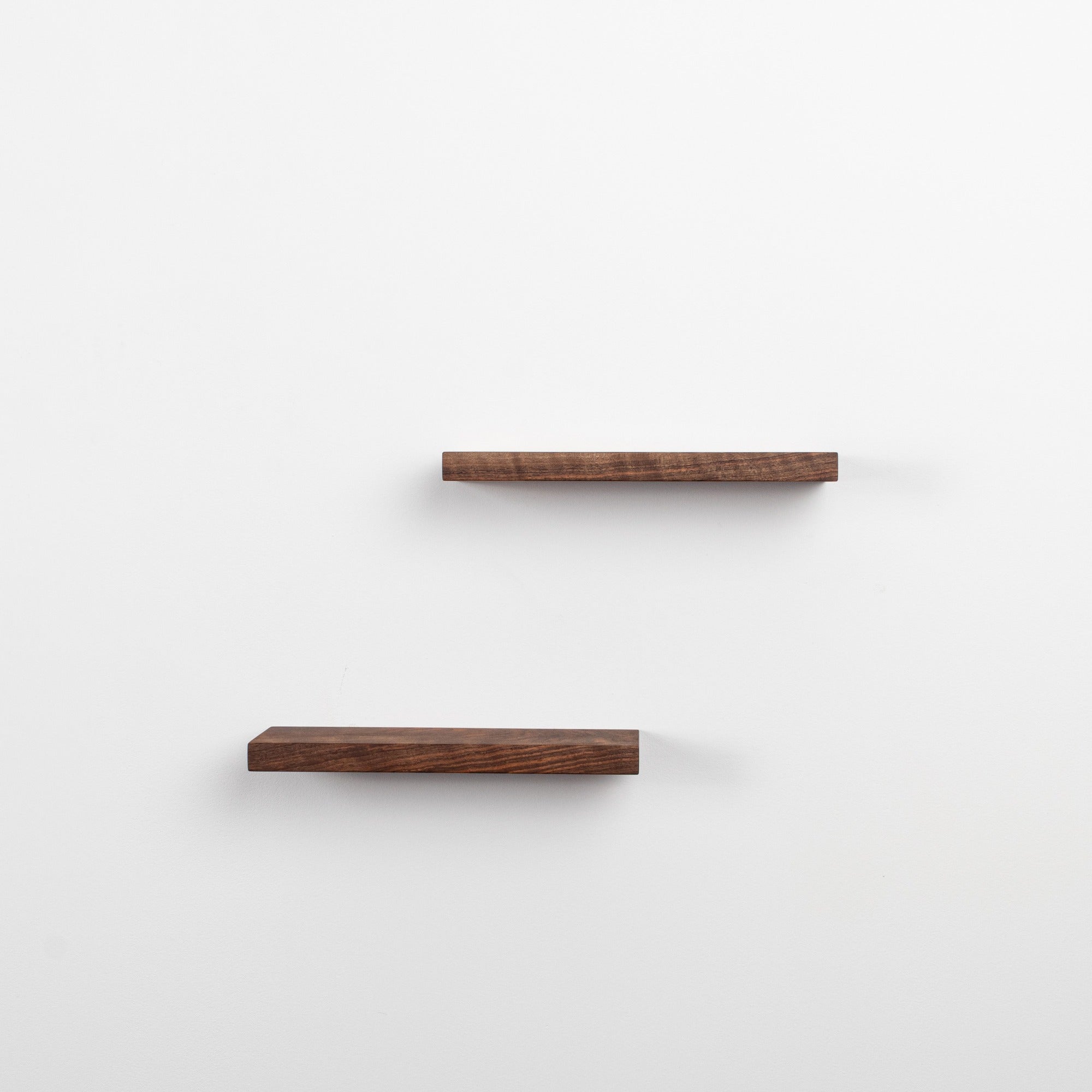 Two wooden shelves on a white wall