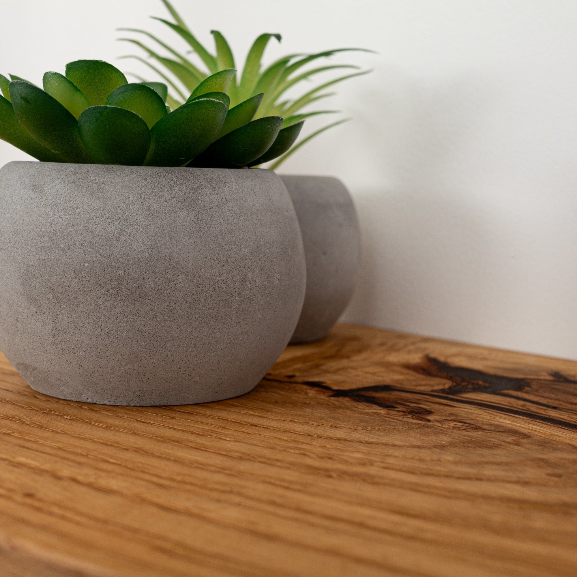 Two gray concrete planters with green plants on a wooden surface.