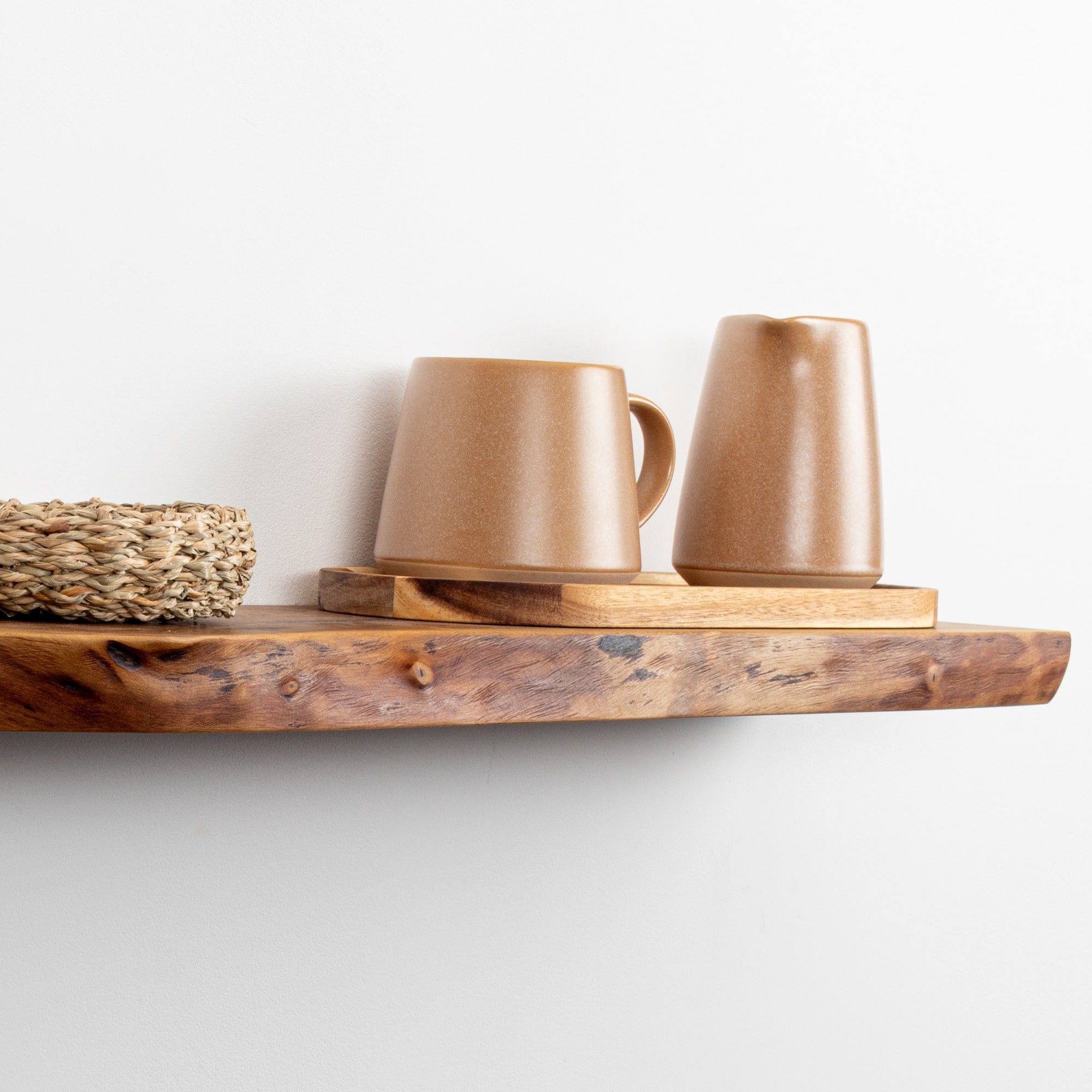 Two brown ceramic mugs on a wooden shelf against a white wall