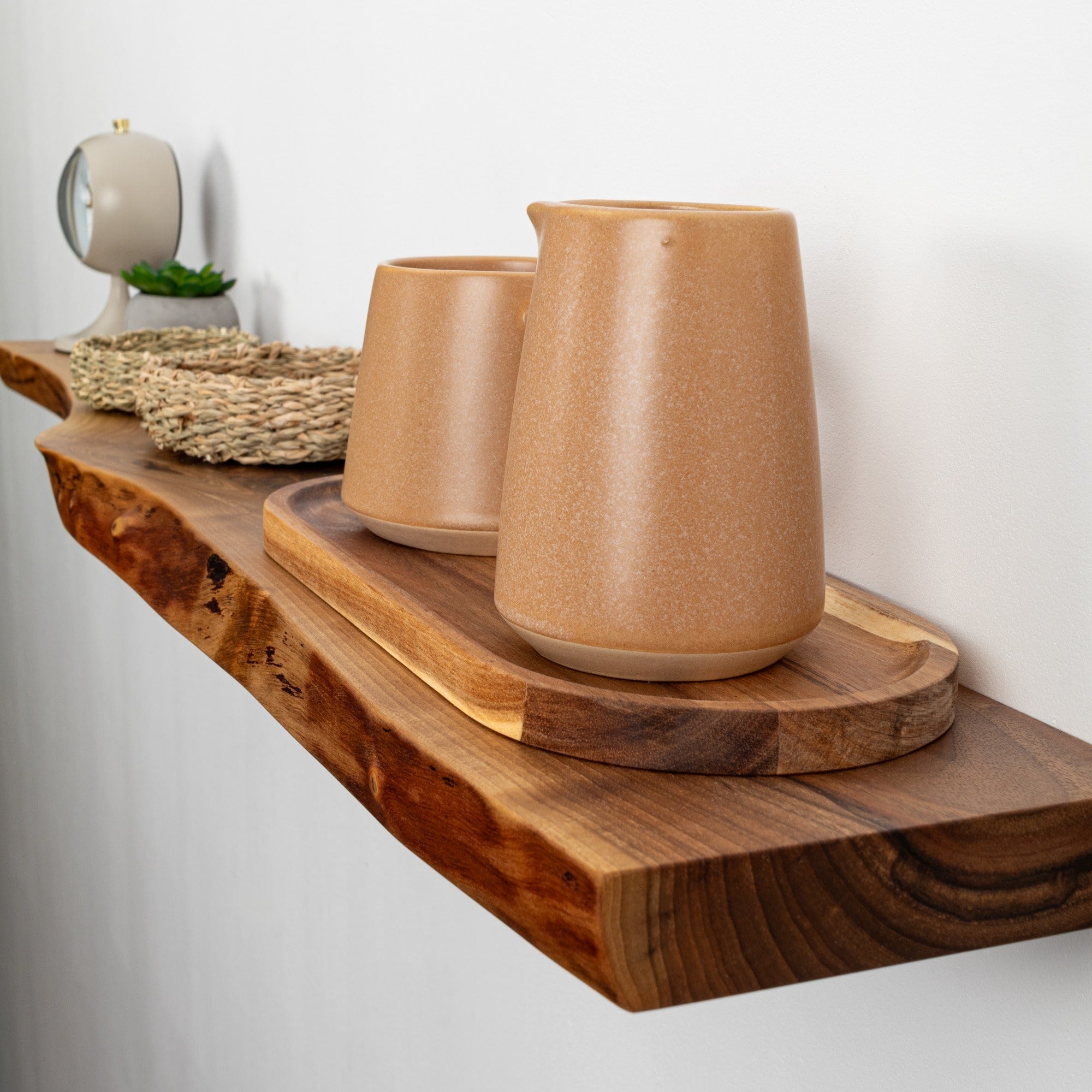 Two brown ceramic cups on a wooden shelf against a white wall.