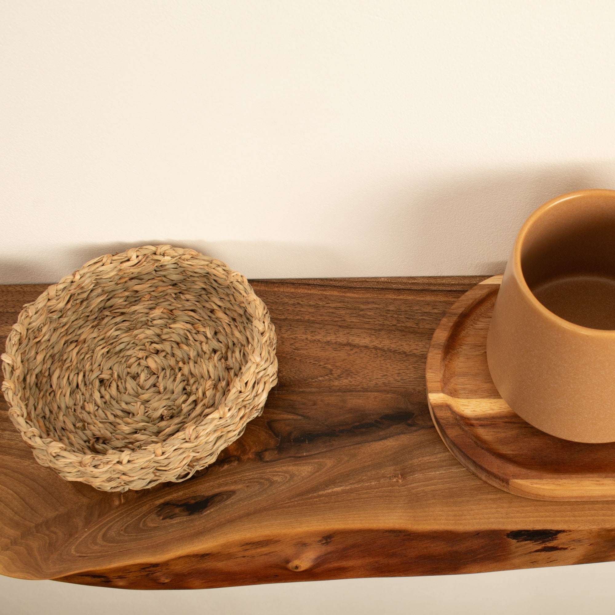 Brown ceramic cup on a wooden coaster with a woven mat on a wooden surface.