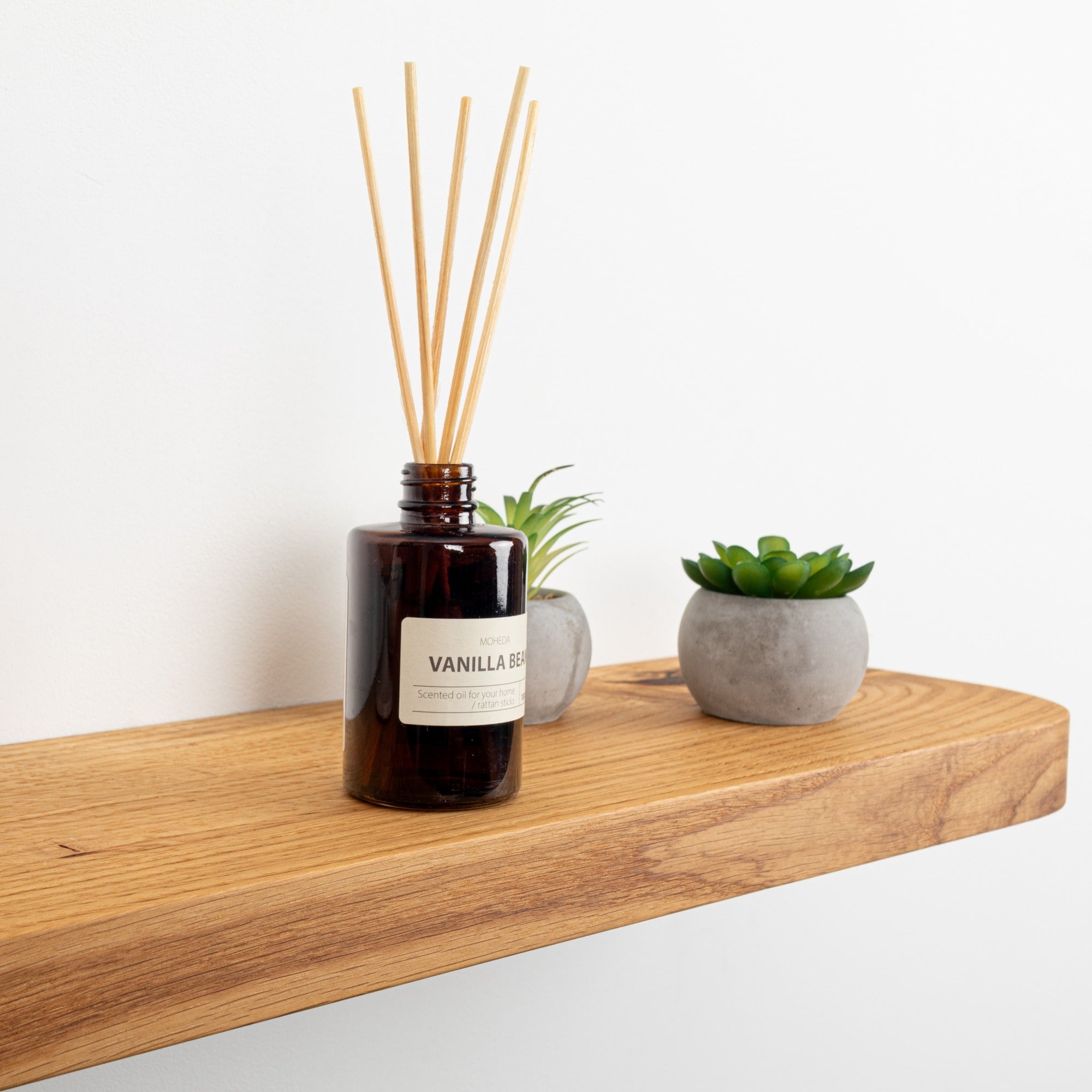 Vanilla reed diffuser on a wooden shelf with small plants