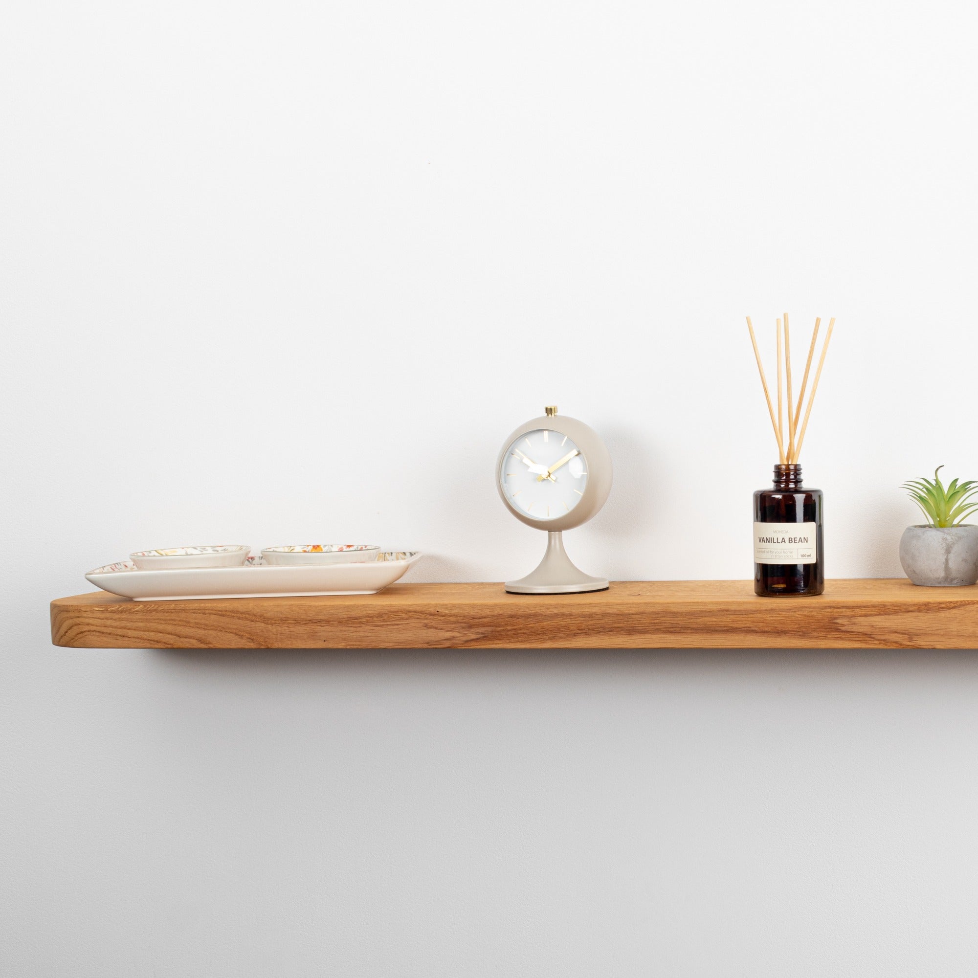 Wooden shelf with decorative items including a plant, bottle, and small clock on a white wall.