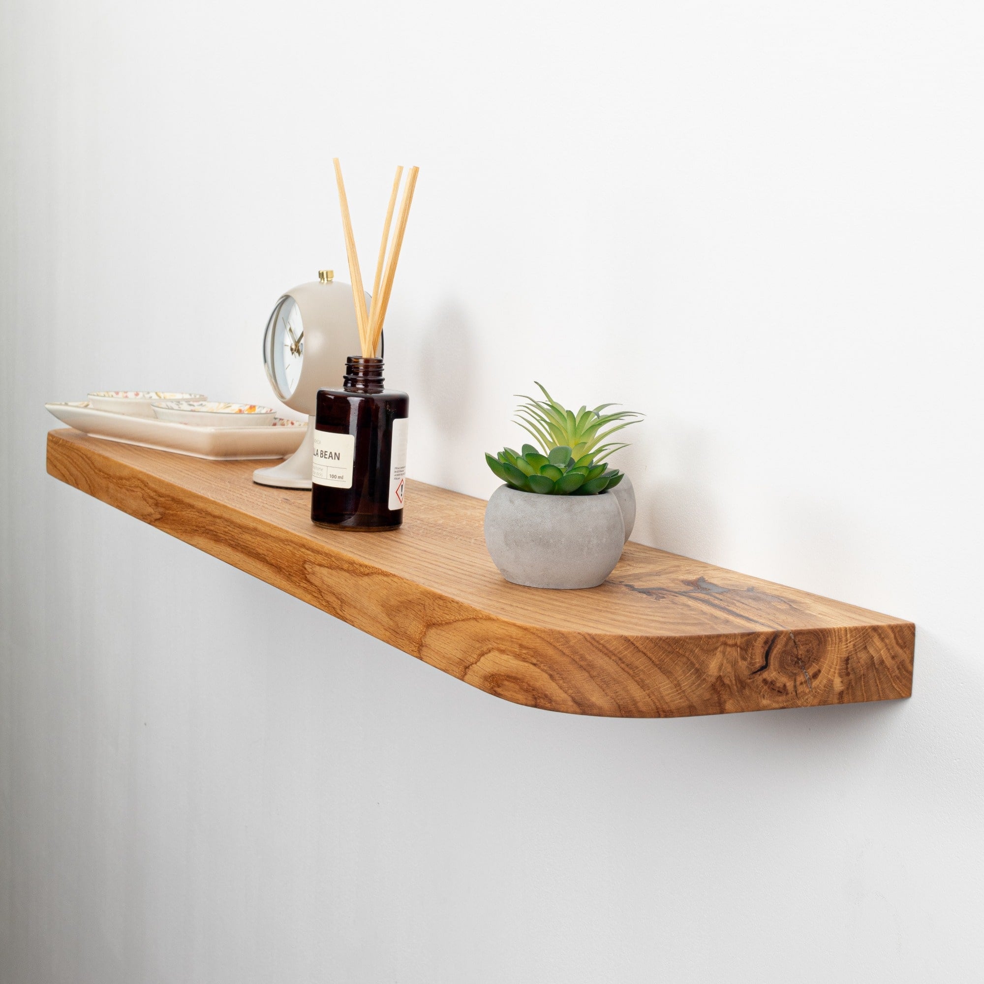 Wooden shelf with decorative items including a plant, diffuser, and bowls on a white wall.