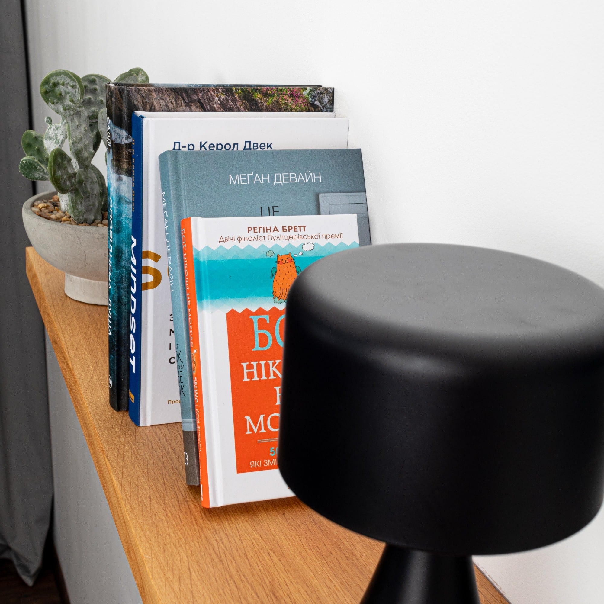 Black stool on a wooden floor with books and a plant in the background