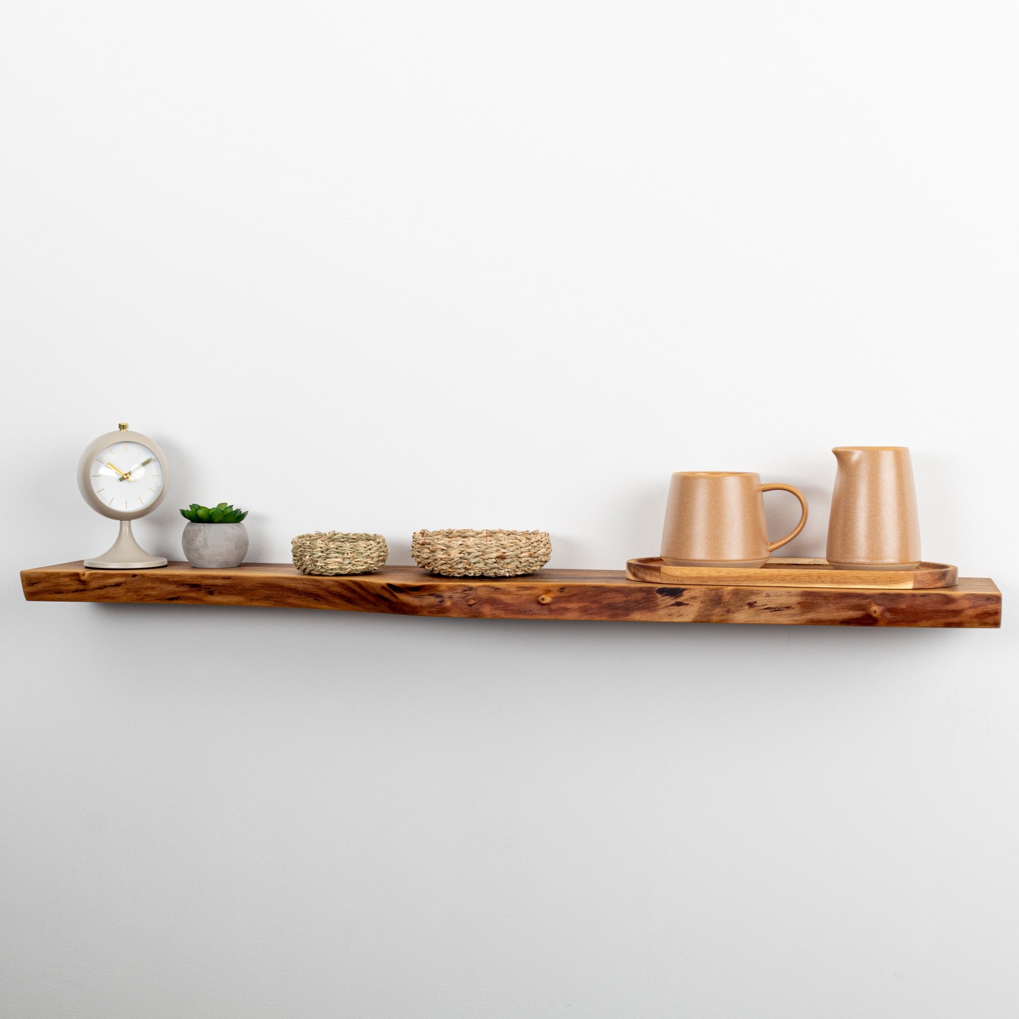 Wooden shelf with decorative items including a clock, plants, and ceramic pieces against a white wall.