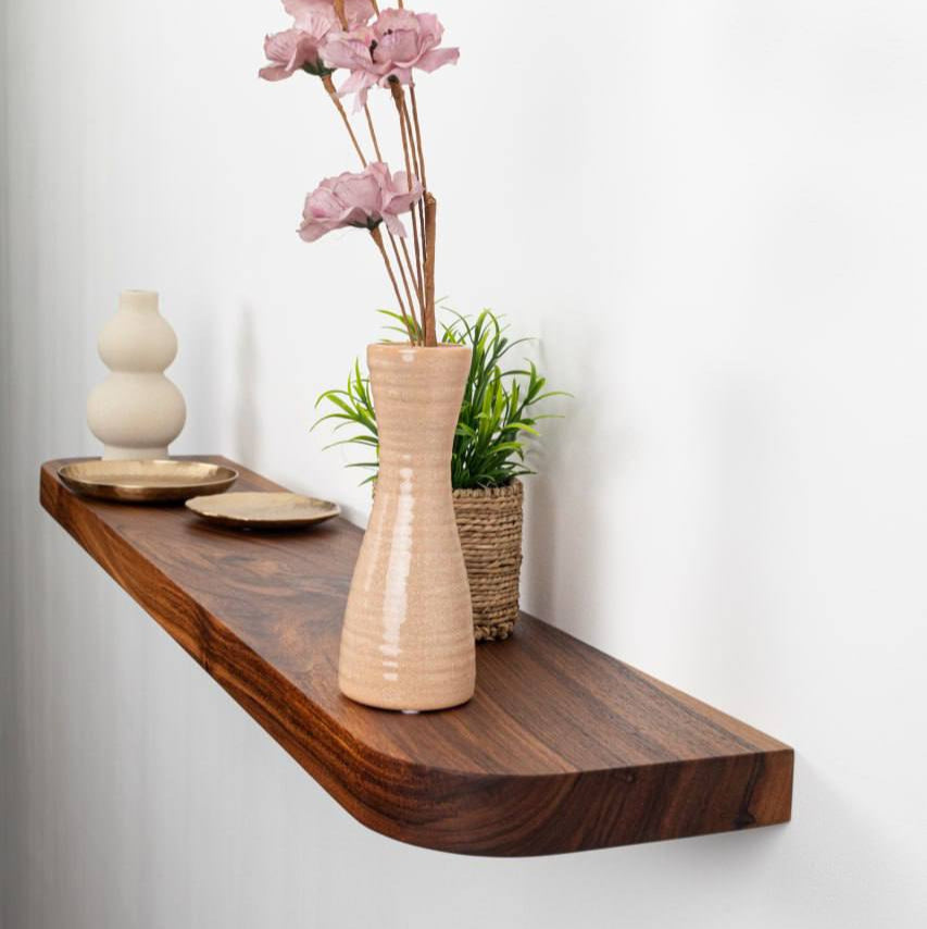 Wooden shelf with decorative items including a vase with pink flowers, a small plant, and a bowl on a white background.