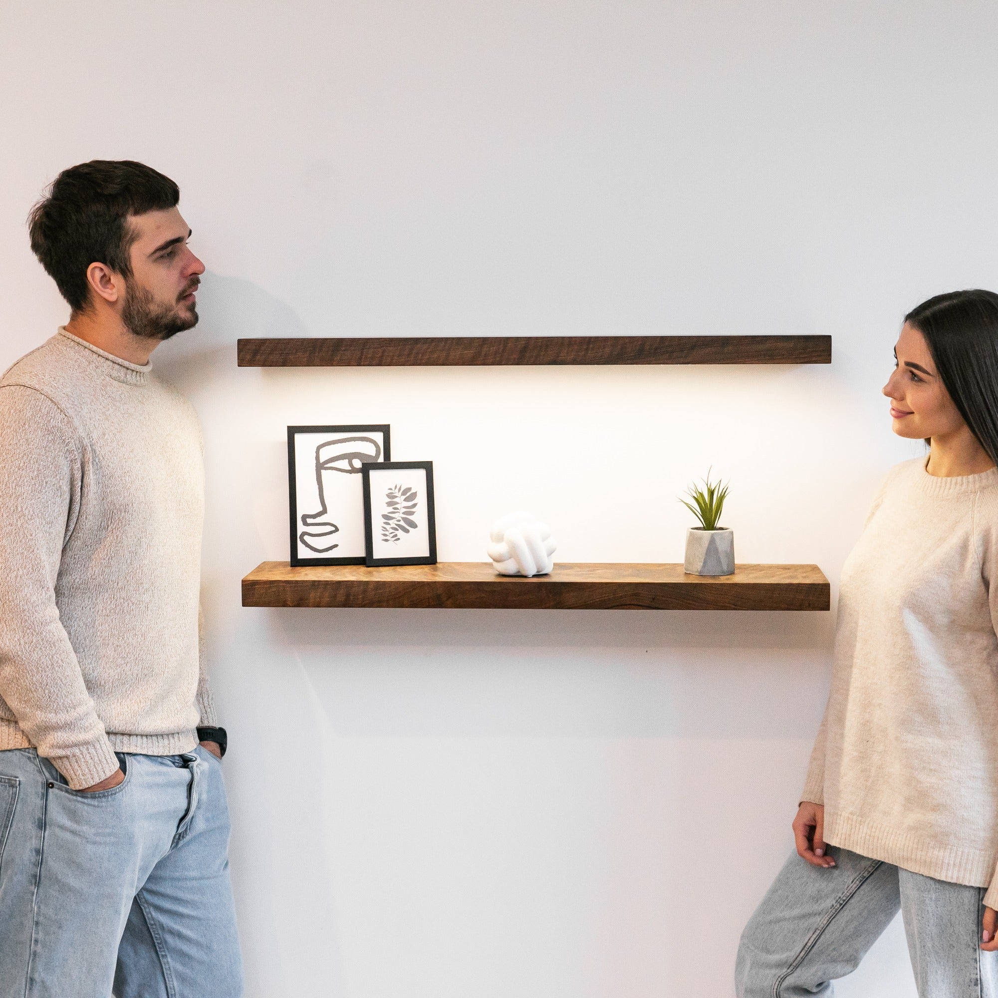 Two people standing in a room with wooden shelves and decor.