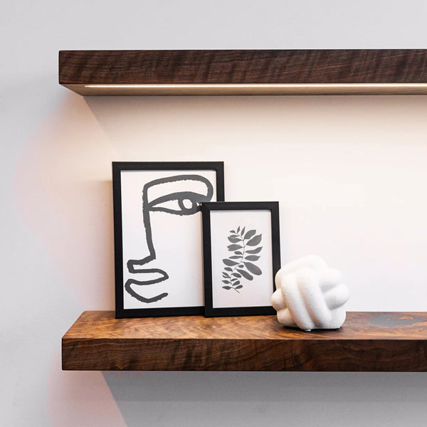 Wooden shelf with framed artwork and a white sculpture against a light wall.