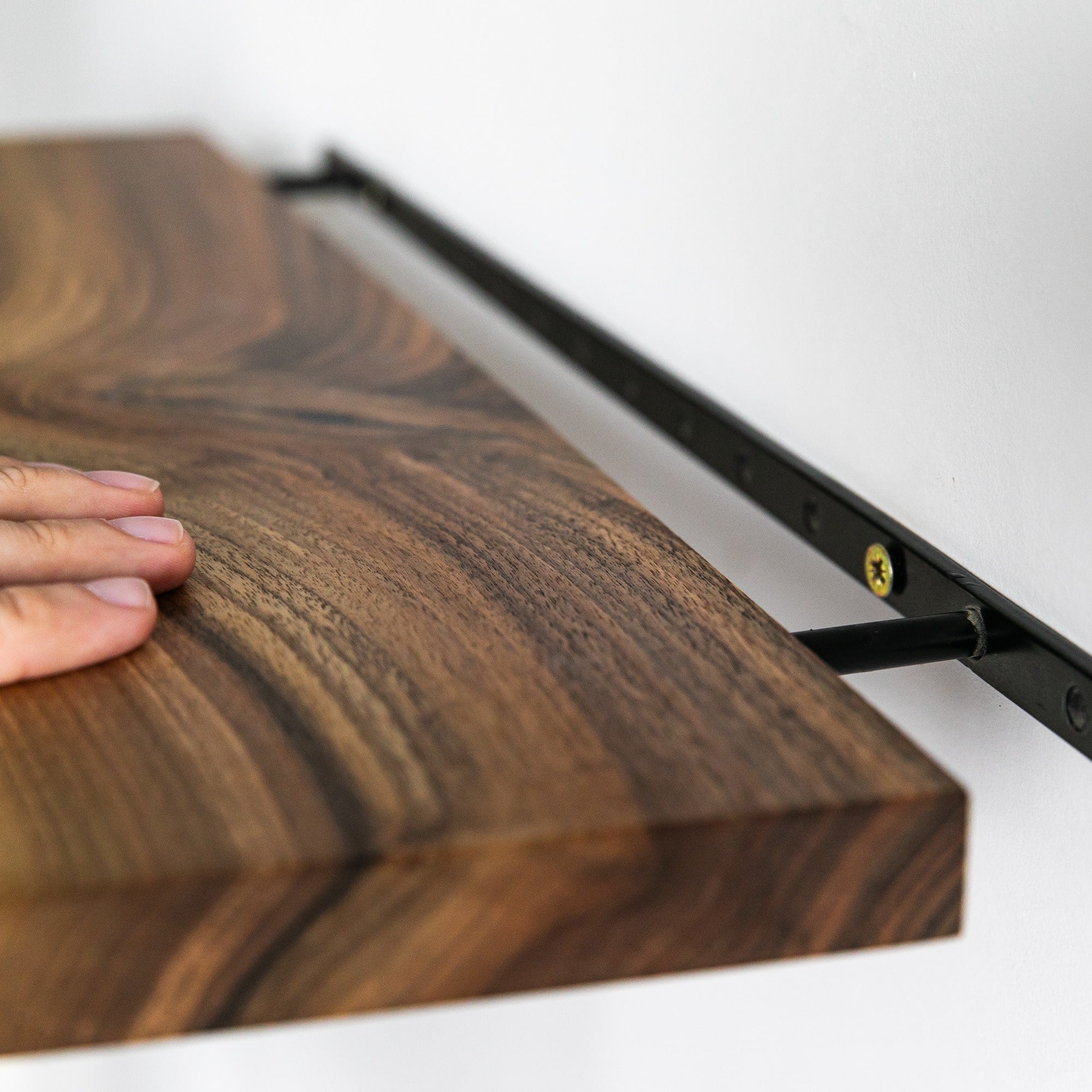 Wooden surface with a hand touching it, mounted on a white wall.