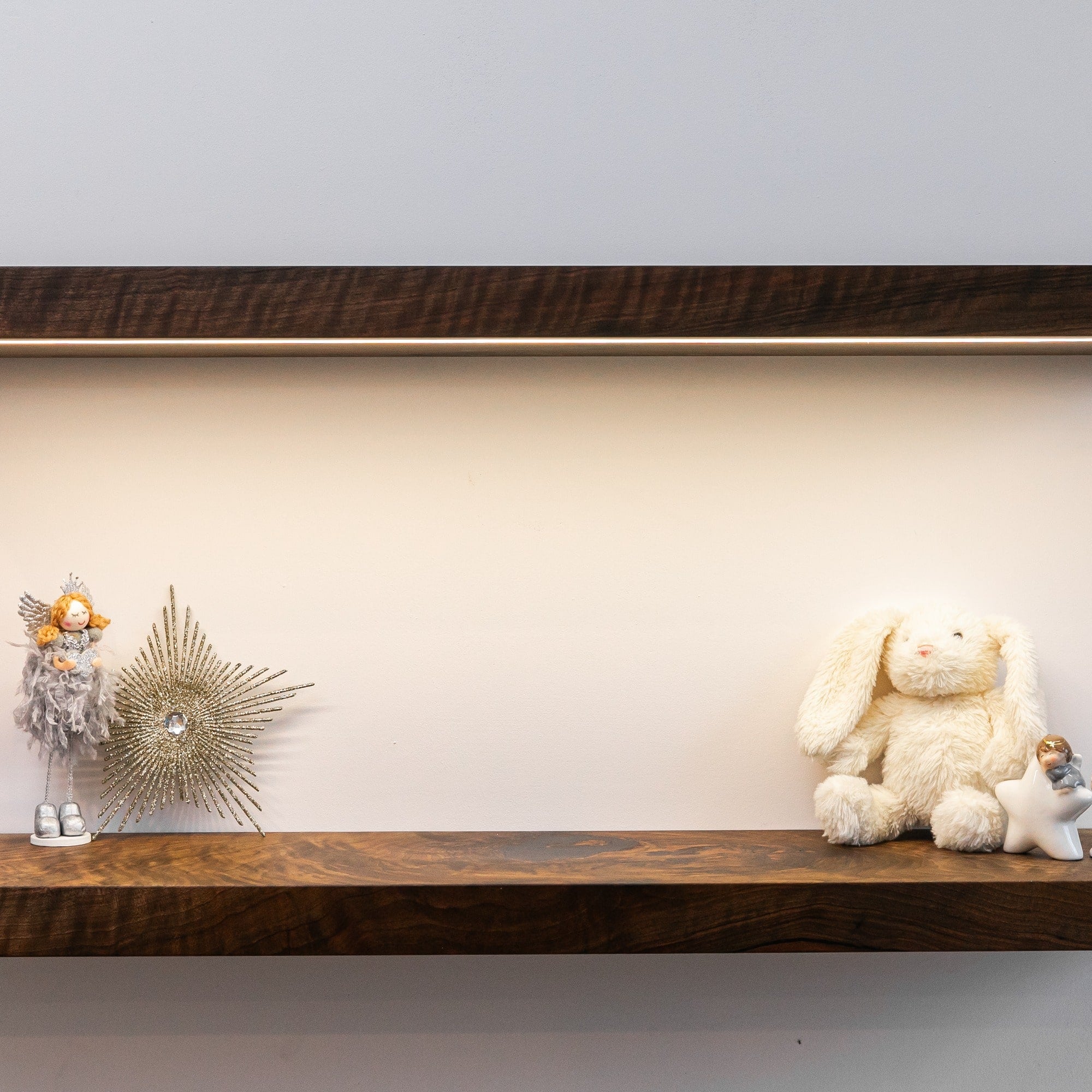 Wooden shelf with decorative items including a teddy bear, angel, and star-shaped object against a plain wall.