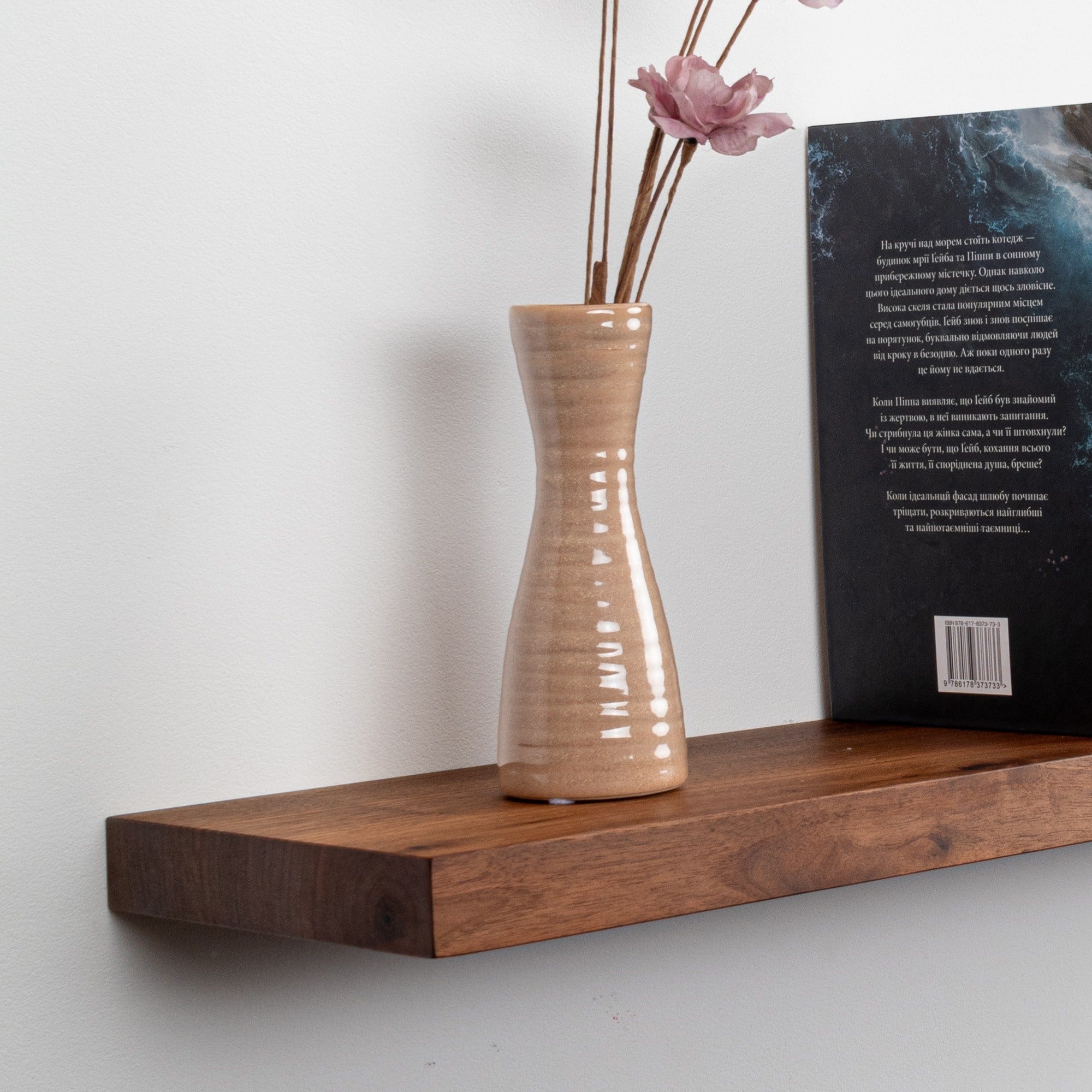 Wooden shelf with a ceramic vase and dried flowers against a white wall.