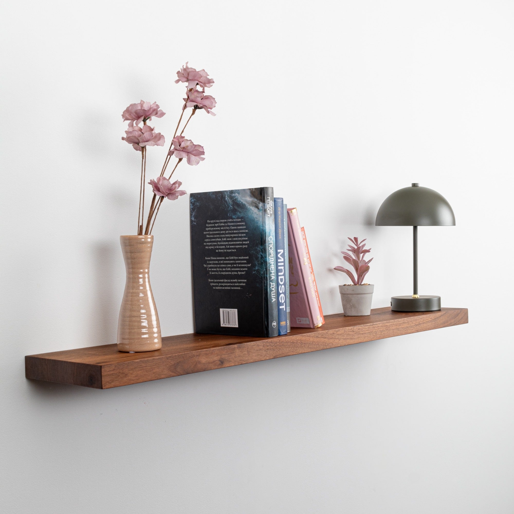 Wooden shelf with decorative items including a vase with flowers, books, and a small lamp against a white wall.